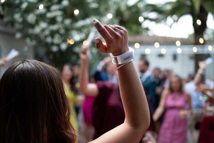 Persona levantando el brazo con una pulsera led blanca en un evento al aire libre, con luces y gente bailando al fondo